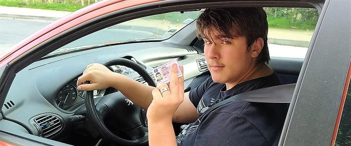 Jeune au volant de sa voiture avec son permi de voiture en main